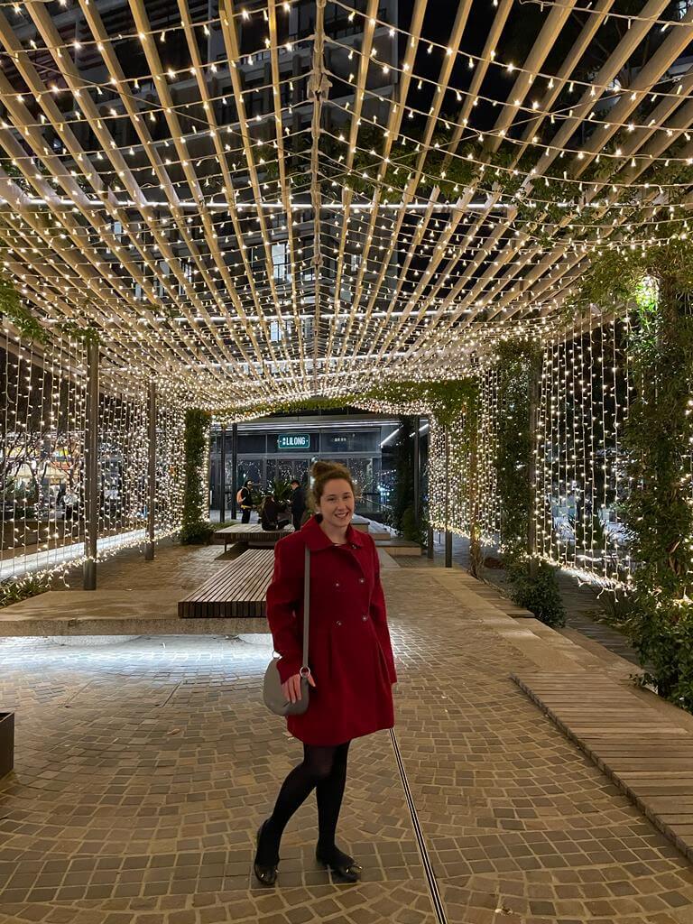 Rebecca standing beneath a tunnel of warm string lights at a winter market in Sydney.