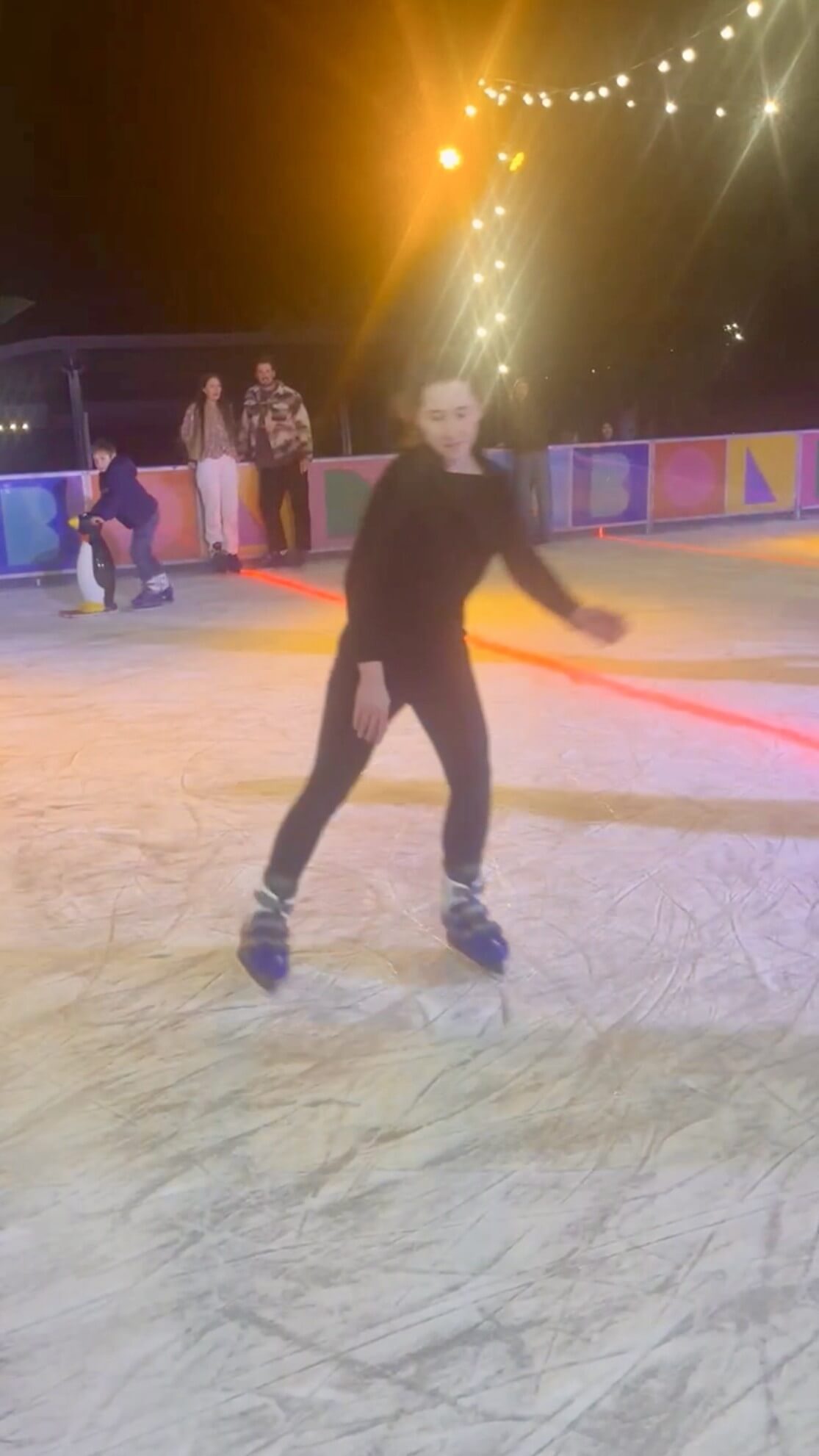 Rebecca ice skating at the Bondi Festival outdoor rink at night under bright string lights.