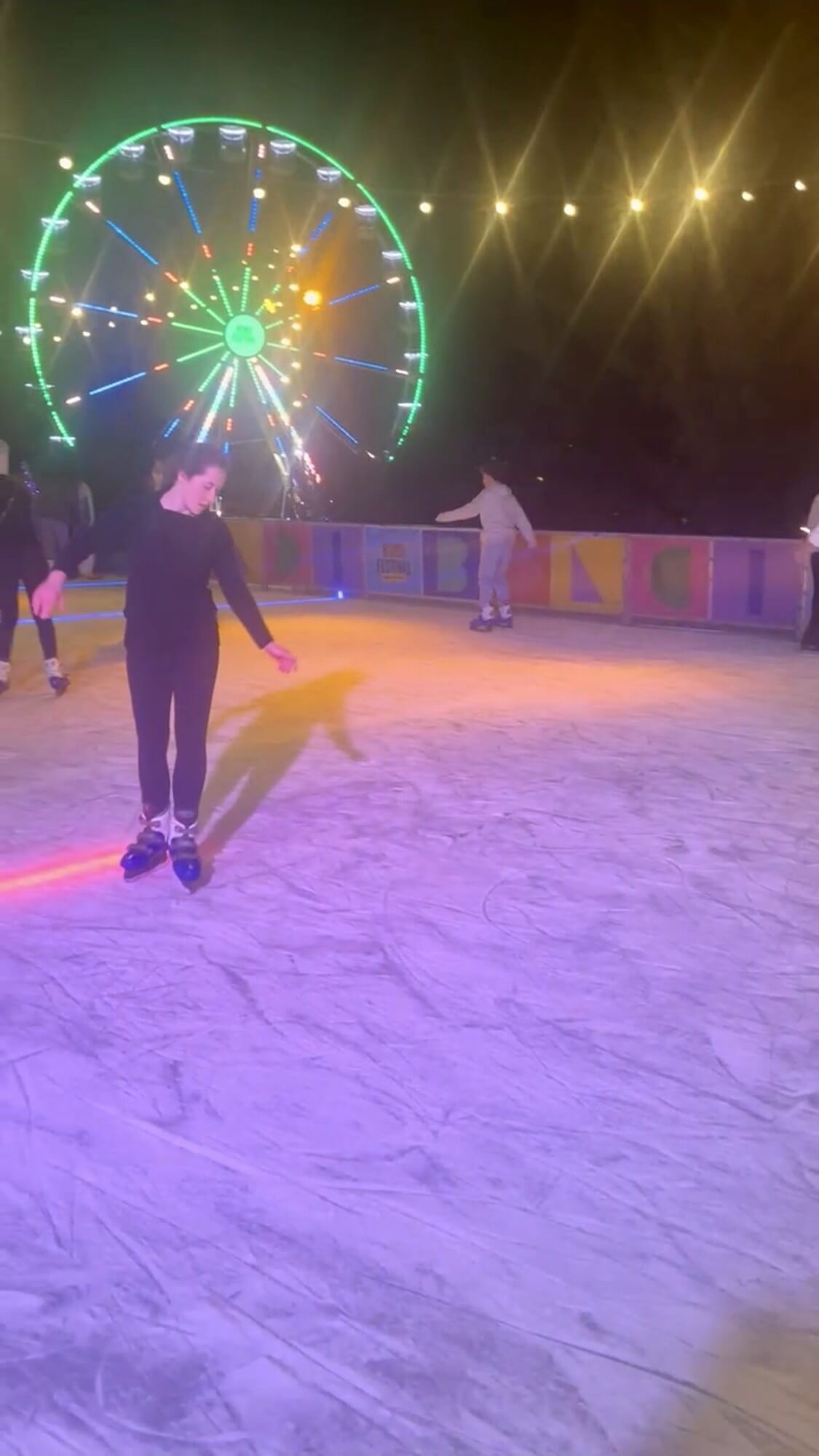 Rebecca ice skating at the Bondi Festival outdoor rink at night with a colourful Ferris wheel glowing in the background.