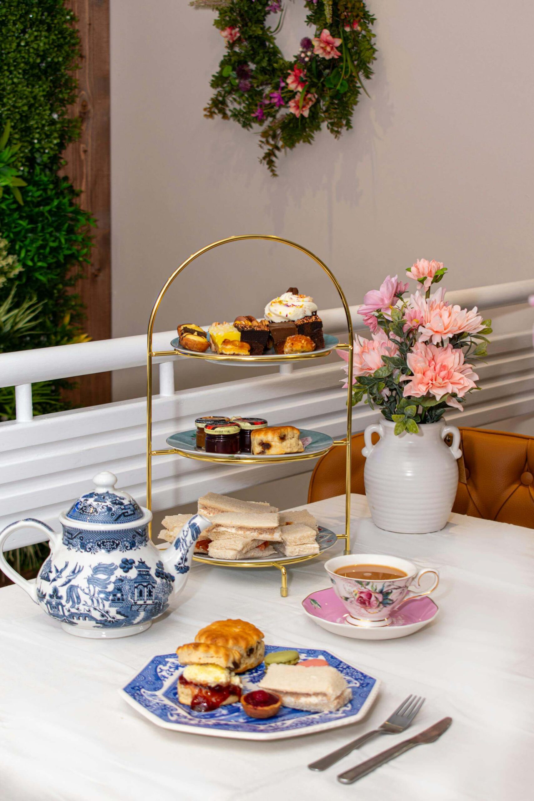 Three-tier high tea stand with scones, finger sandwiches, and pastries served alongside teacups and flowers on a table inside the Queen Victoria Building.