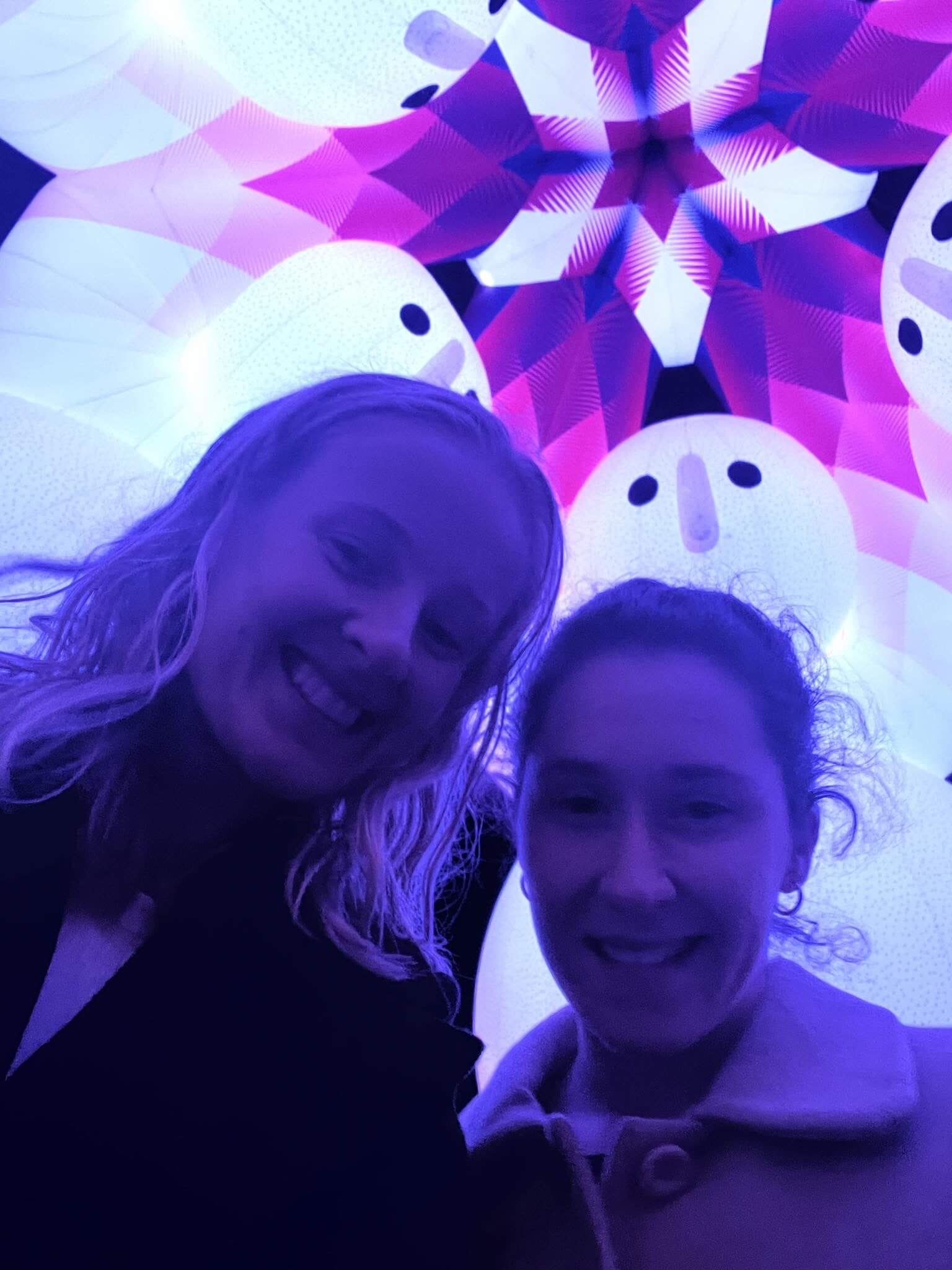 Rebecca and her friend smiling under a colourful glowing Vivid Sydney light installation.