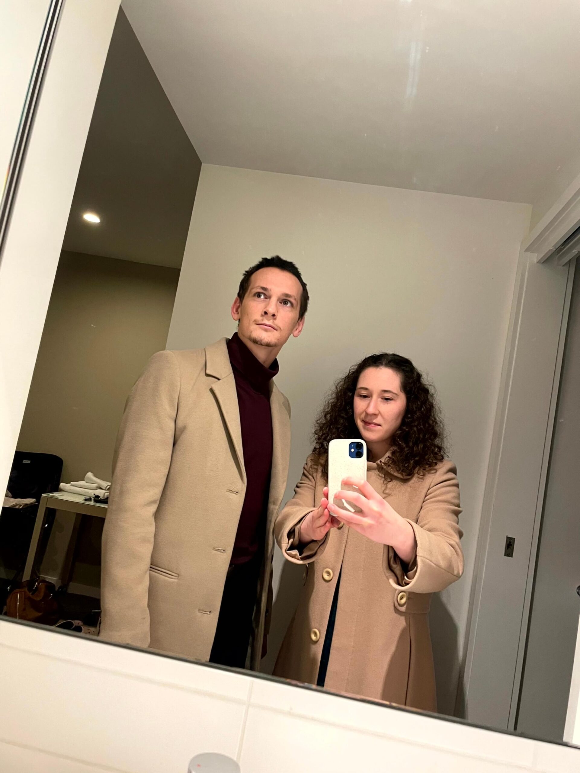Rebecca and her partner Patrick taking a mirror selfie while dressed in coats for a winter night out.
